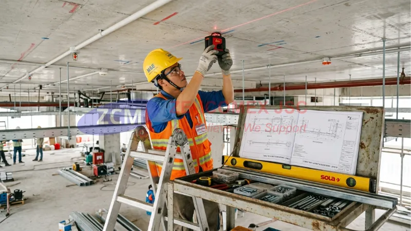 Biện Pháp Thi Công Thang Máng Cáp Điện: Quy Trình & Tiêu Chuẩn M&E 3 Kỹ thuật viên dùng máy laser định vị tuyến thang máng cáp và chuẩn bị lắp giá treo